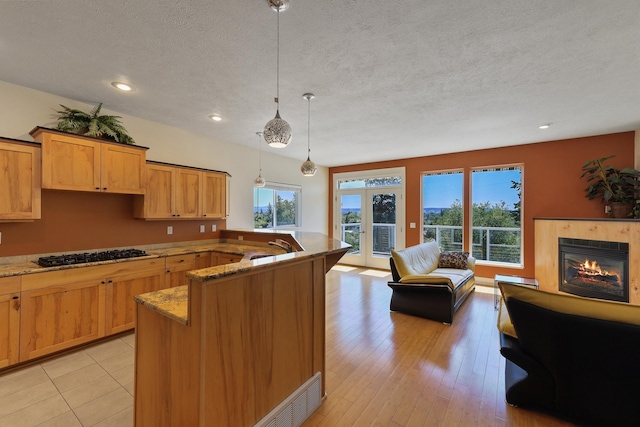 kitchen with french doors, light stone counters, a tile fireplace, decorative light fixtures, and stainless steel gas stovetop