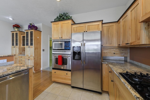 kitchen with light brown cabinets, stone counters, a textured ceiling, appliances with stainless steel finishes, and light tile patterned flooring