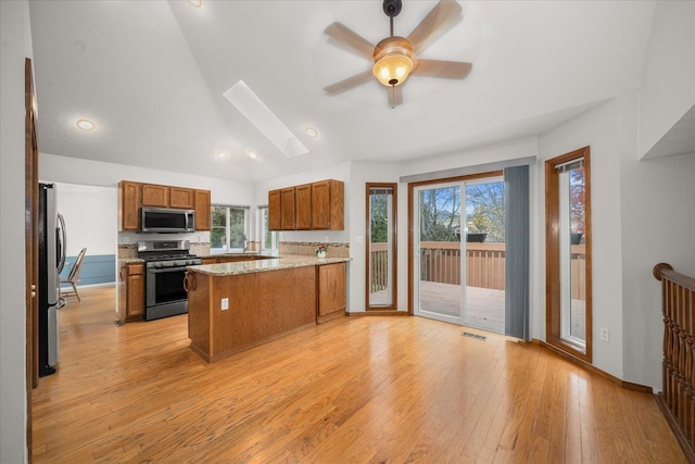 kitchen featuring light stone counters, vaulted ceiling with skylight, stainless steel appliances, ceiling fan, and light hardwood / wood-style floors