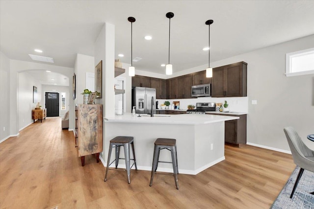 kitchen featuring dark brown cabinetry, stainless steel appliances, kitchen peninsula, a breakfast bar, and light wood-type flooring