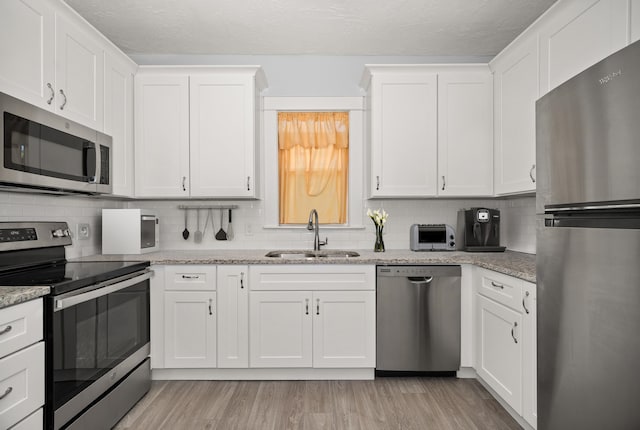 kitchen with light stone counters, appliances with stainless steel finishes, sink, and white cabinets