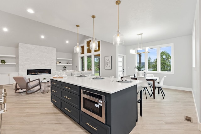 kitchen featuring a kitchen island, a stone fireplace, pendant lighting, built in features, and a breakfast bar area