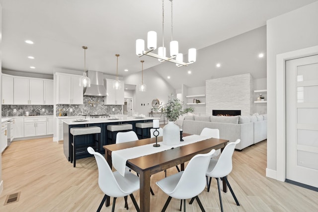 dining room featuring high vaulted ceiling, light wood-type flooring, an inviting chandelier, and a fireplace