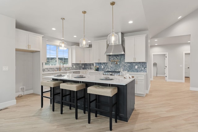 kitchen with wall chimney range hood, a center island, hanging light fixtures, and white cabinets