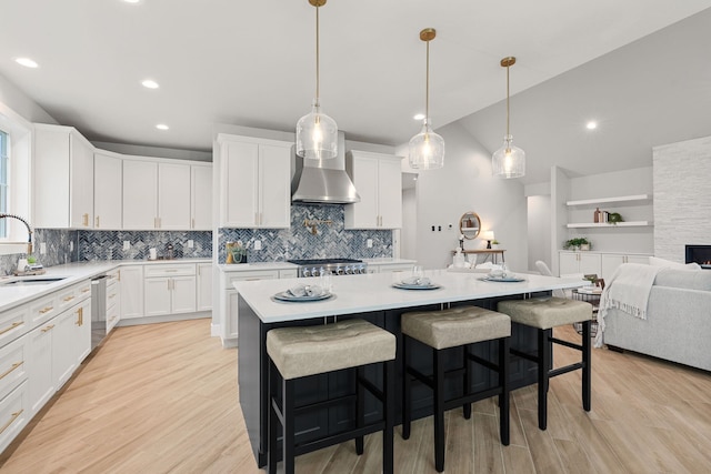 kitchen with light hardwood / wood-style flooring, a kitchen breakfast bar, a kitchen island, wall chimney range hood, and white cabinets