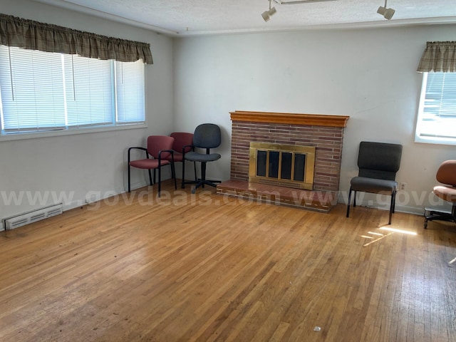 sitting room with a baseboard heating unit, wood-type flooring, a textured ceiling, and a brick fireplace