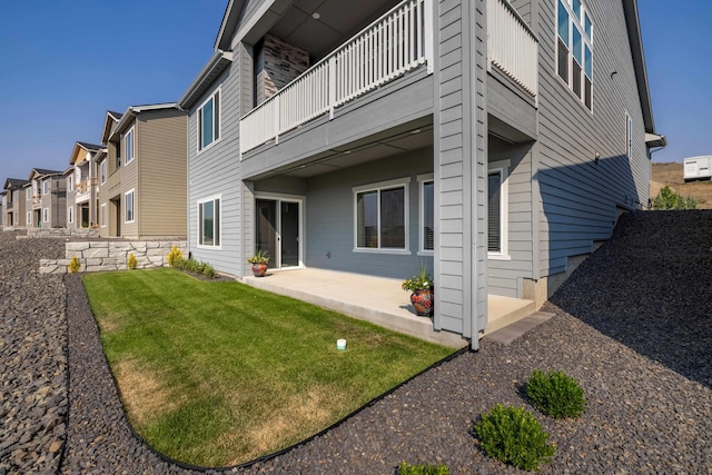 rear view of property featuring a lawn, a balcony, and a patio