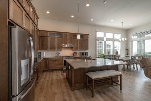 kitchen featuring a kitchen bar, stainless steel appliances, a center island with sink, light hardwood / wood-style floors, and hanging light fixtures