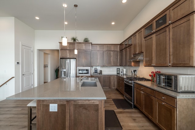 kitchen with dark hardwood / wood-style flooring, stainless steel appliances, a kitchen island with sink, sink, and hanging light fixtures