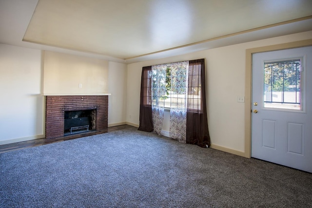 unfurnished living room with dark colored carpet, a raised ceiling, and a brick fireplace