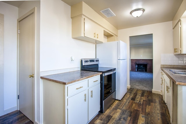 kitchen featuring tasteful backsplash, a brick fireplace, stainless steel electric stove, dark wood-type flooring, and white cabinetry