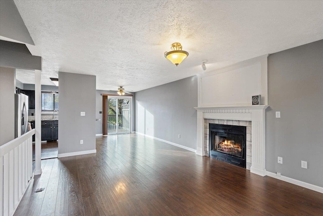 unfurnished living room featuring a textured ceiling, ceiling fan, a fireplace, and dark wood-type flooring