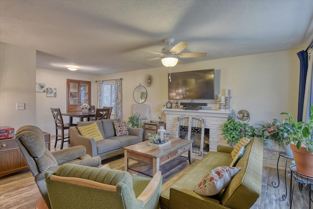 living room with ceiling fan, light wood-type flooring, and a brick fireplace