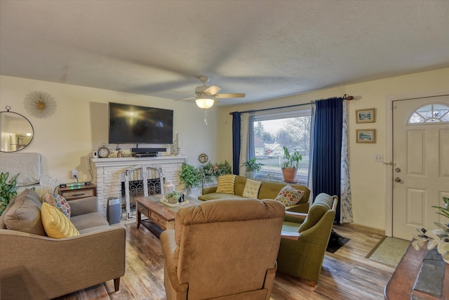 living room with hardwood / wood-style flooring, ceiling fan, a textured ceiling, and a brick fireplace