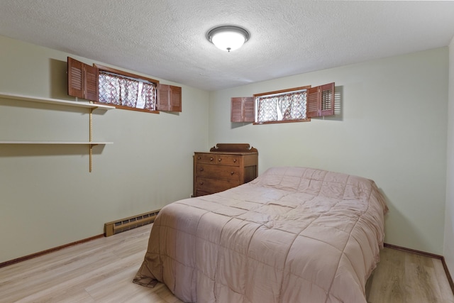 bedroom featuring a textured ceiling, light hardwood / wood-style floors, baseboard heating, and multiple windows