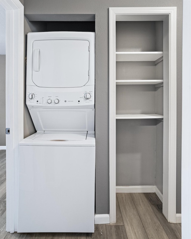 clothes washing area featuring hardwood / wood-style flooring and stacked washer and clothes dryer