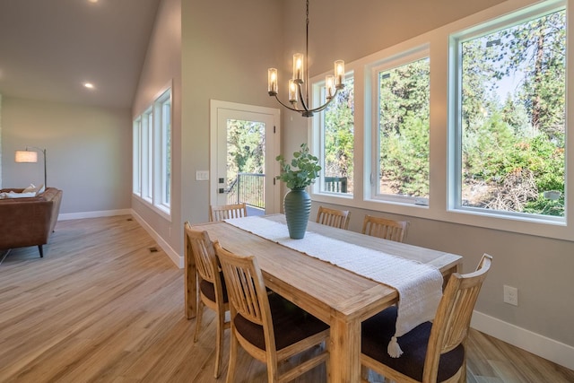 dining area with light wood-type flooring, an inviting chandelier, a wealth of natural light, and lofted ceiling