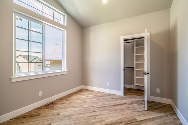 unfurnished bedroom featuring light wood-type flooring, vaulted ceiling, and a closet