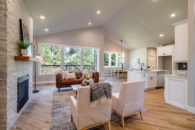 living room with sink, light hardwood / wood-style flooring, vaulted ceiling, and a brick fireplace