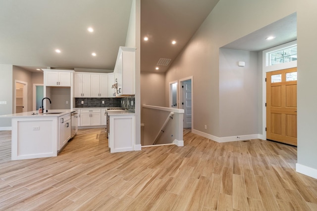 kitchen with high vaulted ceiling, a center island with sink, white cabinets, light wood-type flooring, and tasteful backsplash