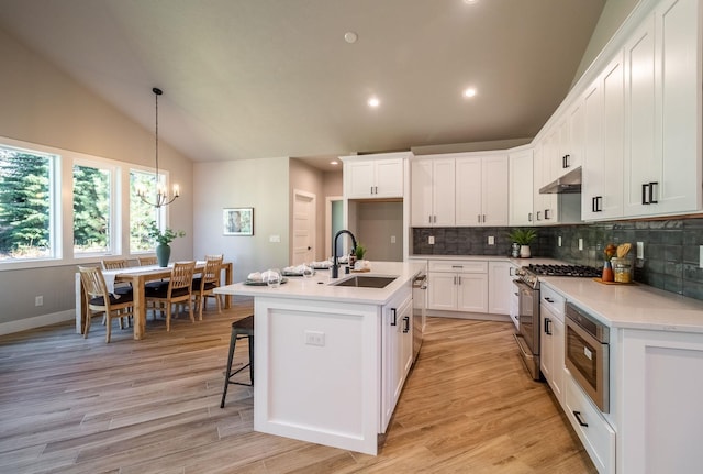 kitchen featuring lofted ceiling, a center island with sink, sink, appliances with stainless steel finishes, and white cabinetry