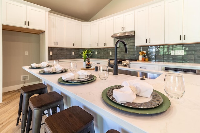 kitchen with a breakfast bar, light stone counters, white cabinetry, and vaulted ceiling