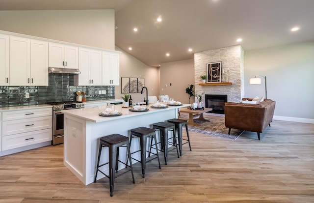 kitchen with a breakfast bar, stainless steel range oven, a fireplace, white cabinetry, and an island with sink