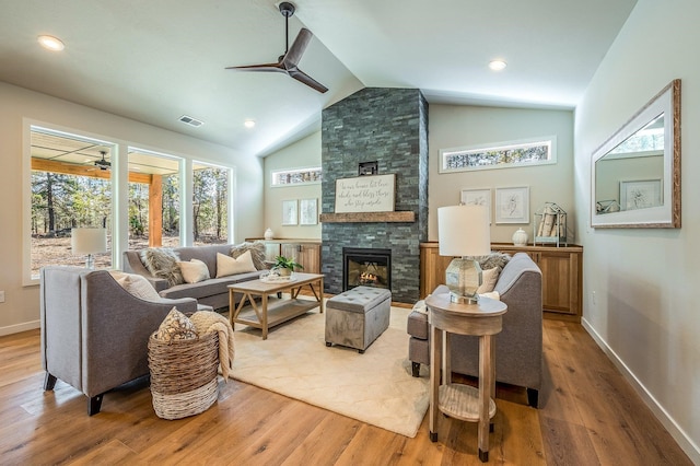 living room featuring ceiling fan, vaulted ceiling, a fireplace, and light hardwood / wood-style flooring