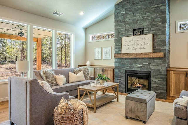 interior space featuring ceiling fan, light hardwood / wood-style floors, a stone fireplace, and vaulted ceiling