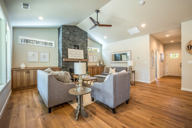 living room with a stone fireplace, ceiling fan, plenty of natural light, and light hardwood / wood-style floors