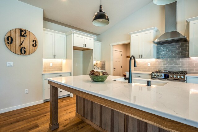 kitchen featuring wall chimney exhaust hood, stainless steel gas stove, decorative light fixtures, light stone counters, and white cabinetry