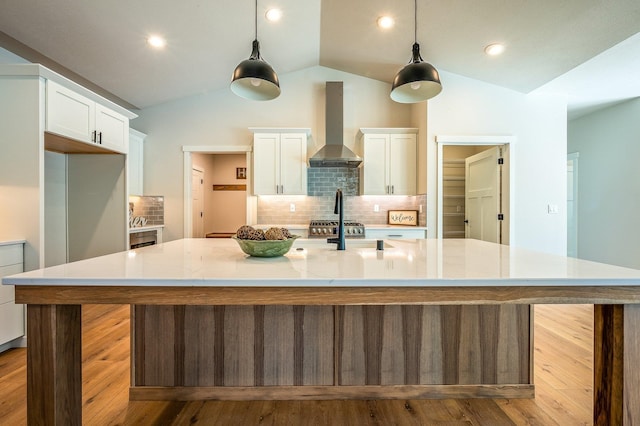 kitchen featuring lofted ceiling, backsplash, a spacious island, wall chimney exhaust hood, and decorative light fixtures