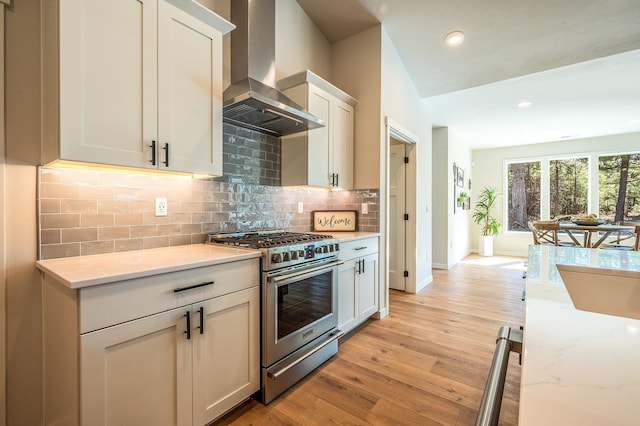 kitchen with light stone counters, light hardwood / wood-style floors, wall chimney range hood, white cabinets, and stainless steel stove