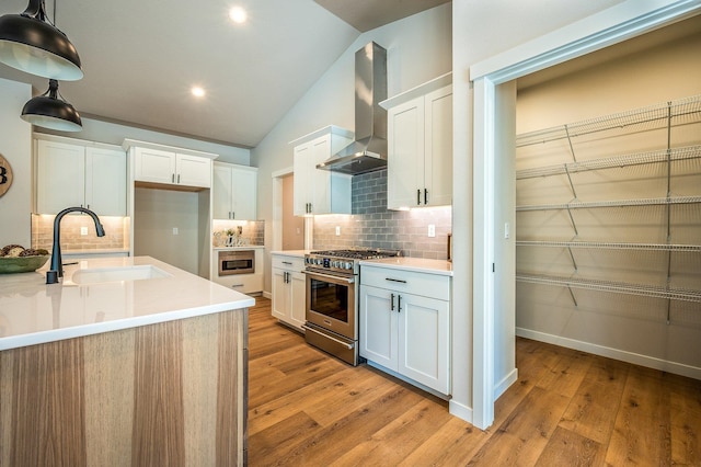 kitchen with high end stove, sink, wall chimney range hood, pendant lighting, and white cabinetry