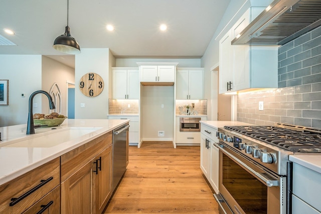 kitchen featuring appliances with stainless steel finishes, wall chimney exhaust hood, sink, decorative light fixtures, and white cabinets