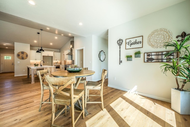 dining space with vaulted ceiling, light hardwood / wood-style flooring, and sink