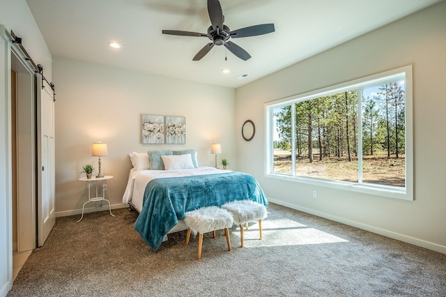 bedroom featuring a barn door, ceiling fan, and dark colored carpet