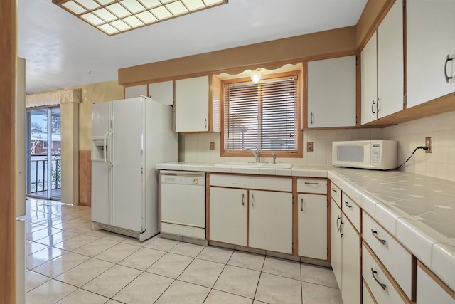 kitchen with sink, white appliances, white cabinets, and tile counters