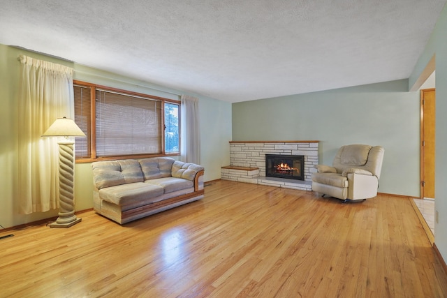 living room featuring light wood-type flooring, a textured ceiling, and a stone fireplace