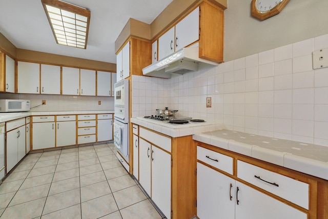 kitchen with white appliances, tasteful backsplash, white cabinetry, light tile patterned floors, and tile countertops