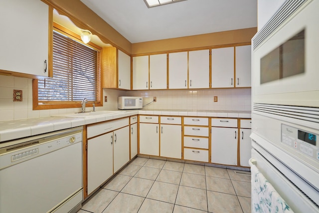 kitchen with sink, white cabinetry, light tile patterned flooring, white appliances, and tile counters