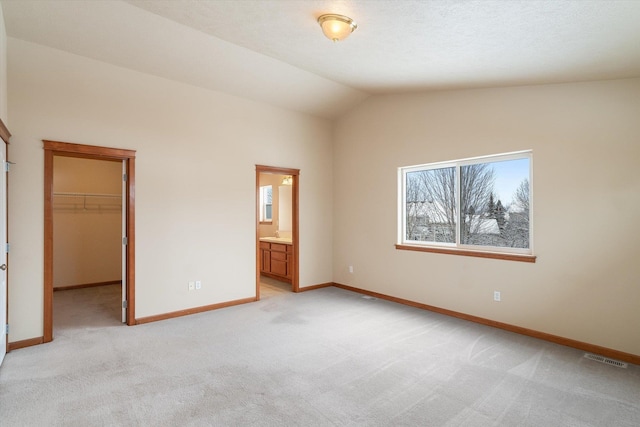 unfurnished bedroom with ensuite bathroom, light colored carpet, vaulted ceiling, a spacious closet, and a closet