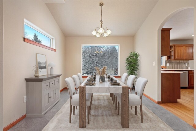 dining room featuring vaulted ceiling, light colored carpet, and a chandelier