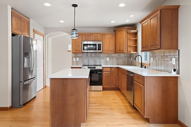 kitchen featuring sink, a center island, decorative light fixtures, appliances with stainless steel finishes, and light wood-type flooring