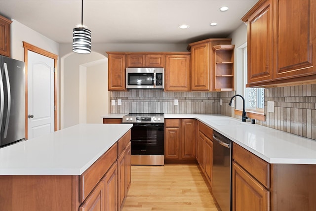 kitchen with sink, appliances with stainless steel finishes, decorative light fixtures, a kitchen island, and light wood-type flooring