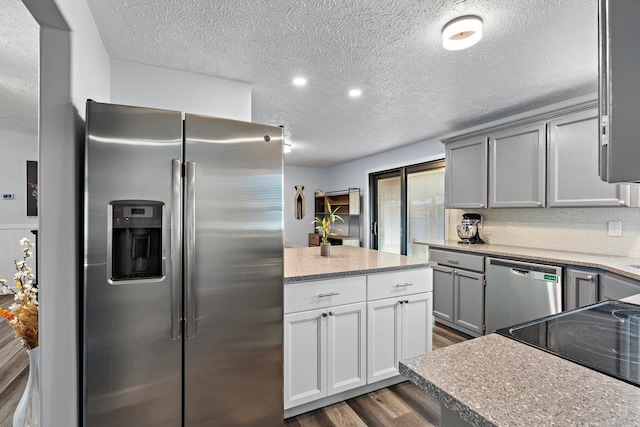 kitchen with gray cabinetry, dark wood-type flooring, stainless steel appliances, a textured ceiling, and decorative backsplash