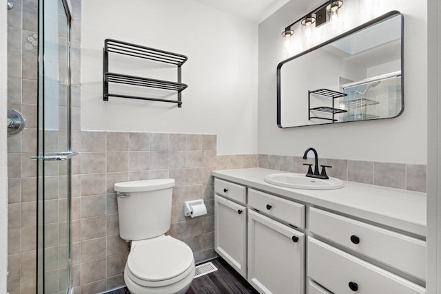 bathroom with vanity, a shower with door, toilet, and tile walls