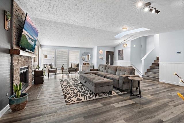 living room featuring a stone fireplace, lofted ceiling with skylight, and wood-type flooring