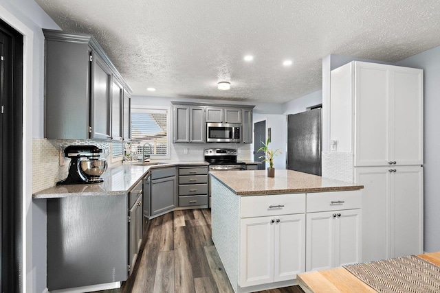 kitchen with gray cabinetry, stainless steel appliances, dark hardwood / wood-style floors, backsplash, and a textured ceiling