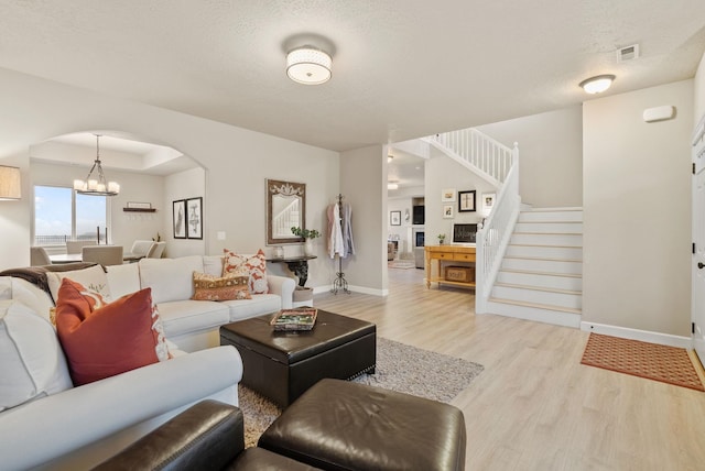 living room featuring a textured ceiling, a tray ceiling, light hardwood / wood-style flooring, and an inviting chandelier